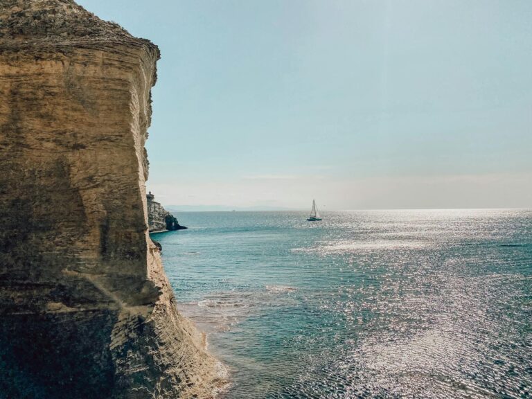 Bateau voguant sur la mer au coucher de soleil, entouré par de hautes falaises Corses