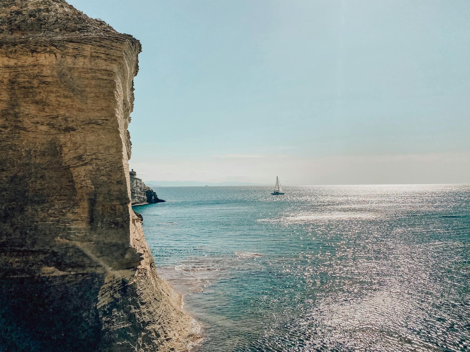 Bateau voguant sur la mer au coucher de soleil, entouré par de hautes falaises Corses
