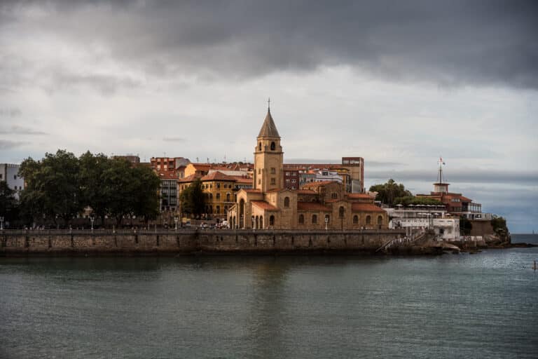 Vue sur l’église San Pedro et le front de mer de Gijón, sous un ciel nuageux.