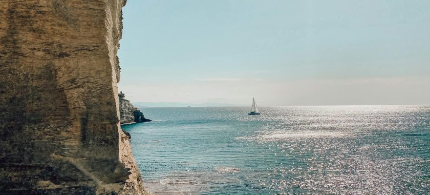 Bateau voguant sur la mer au coucher de soleil, entouré par de hautes falaises Corses